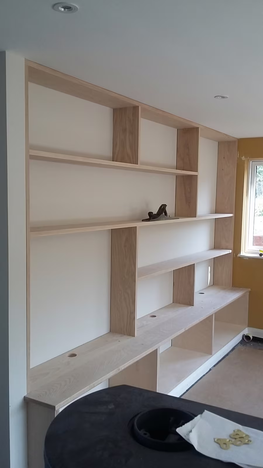 A built-in oak bookcase filling a wall, with cupboards along the bottom and a hand plane resting on a shelf