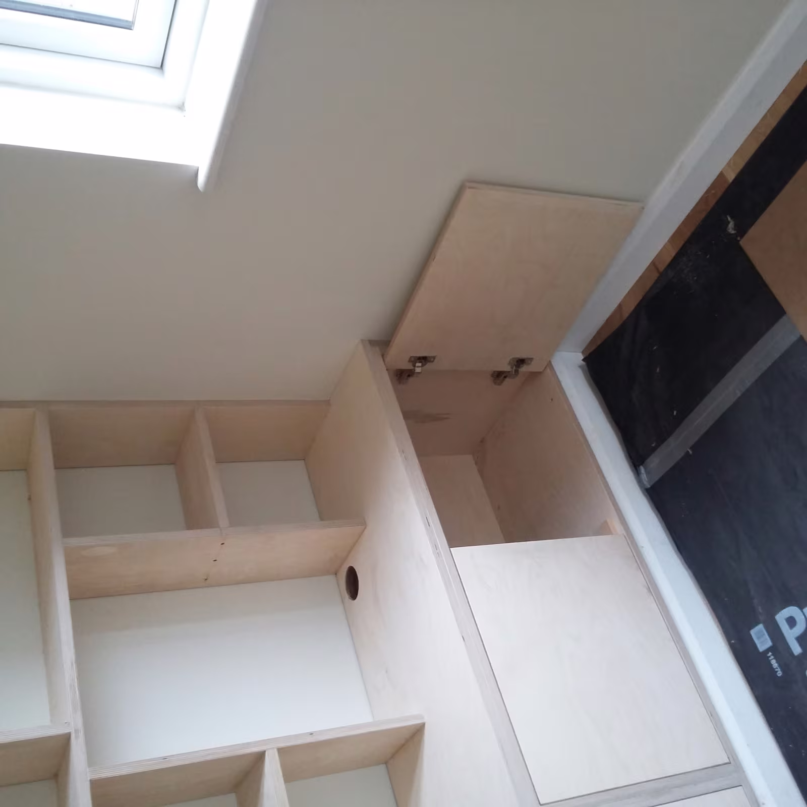 Birch plywood shelving and a lift-up storage hatch built into the eaves of a loft room under a rooflight