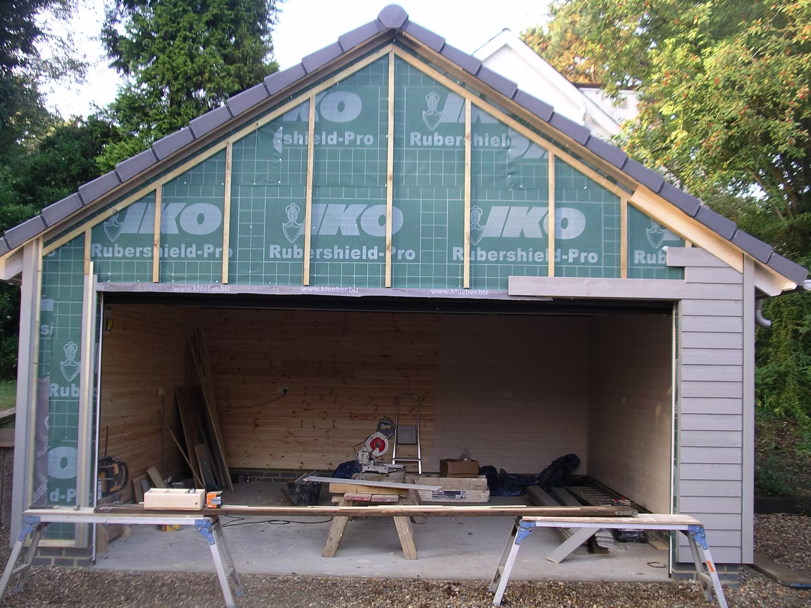 A timber garage taking shape, the gable wrapped in breather membrane and the sides clad in grey weatherboard