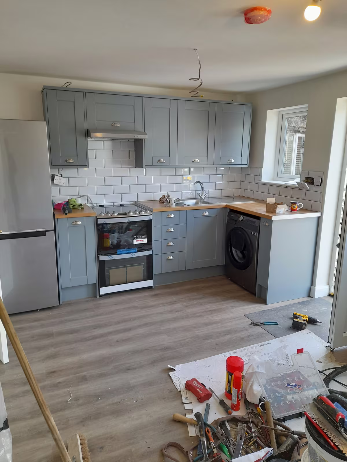 A newly fitted kitchen with grey shaker units, a wooden worktop and white metro tiles, tools still on the floor