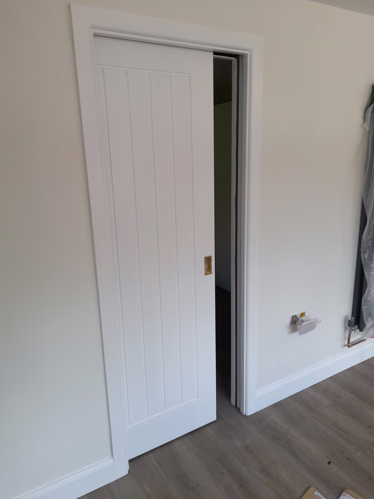 A white panelled pocket door half slid into the wall, with new architrave and skirting